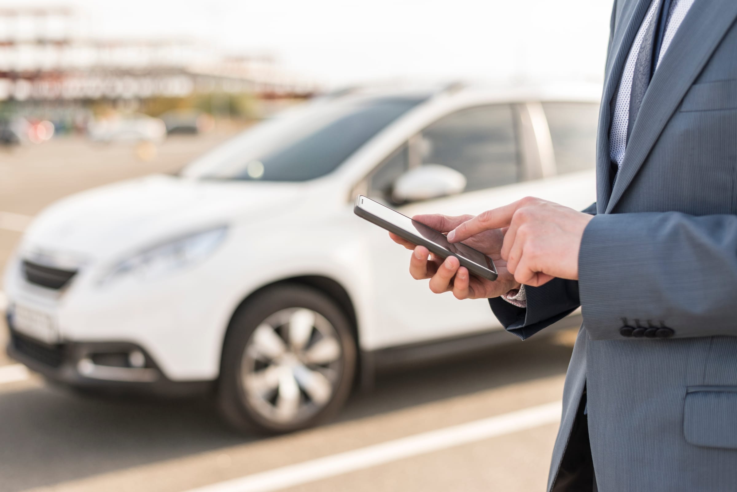 Cadre consultant son smartphone à côté d'un véhicule de location